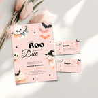 A Halloween baby shower invitation set with a light blue card and matching envelopes, decorated with cartoon ghosts, bats, cupcakes, and a witch, styled on a white surface with pink tulips.