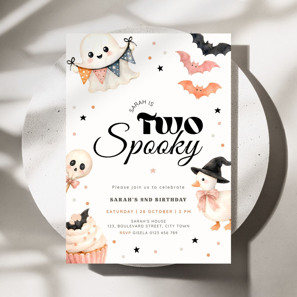 A Halloween-themed birthday invitation card for Sarah's 2nd birthday, styled on a white ceramic plate with soft shadows. The card features cute watercolor illustrations of a ghost, a pumpkin, a skull, a cupcake, and bats on a white background with black and orange text.