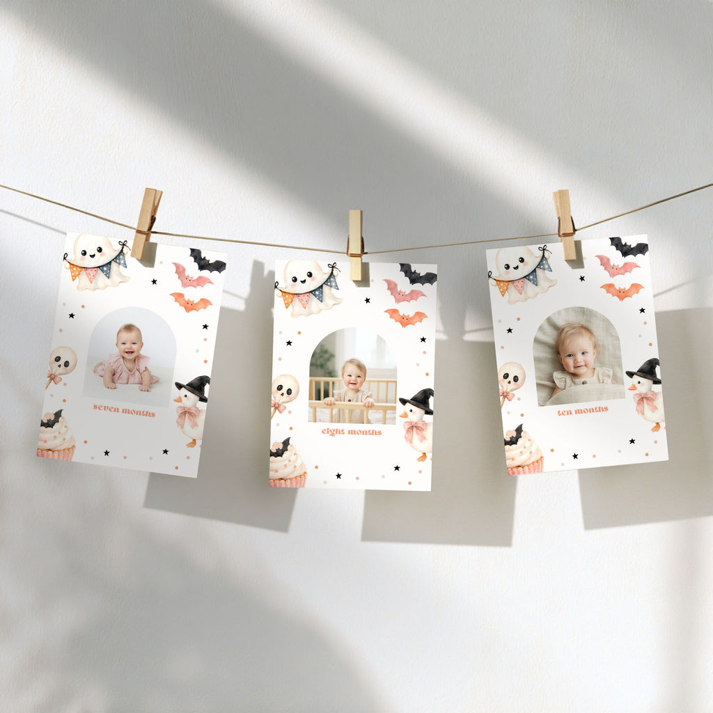 Three personalized Halloween photo cards clipped to a string against a white wall, decorated with cute cartoon illustrations of ghosts, bats, and cupcakes.