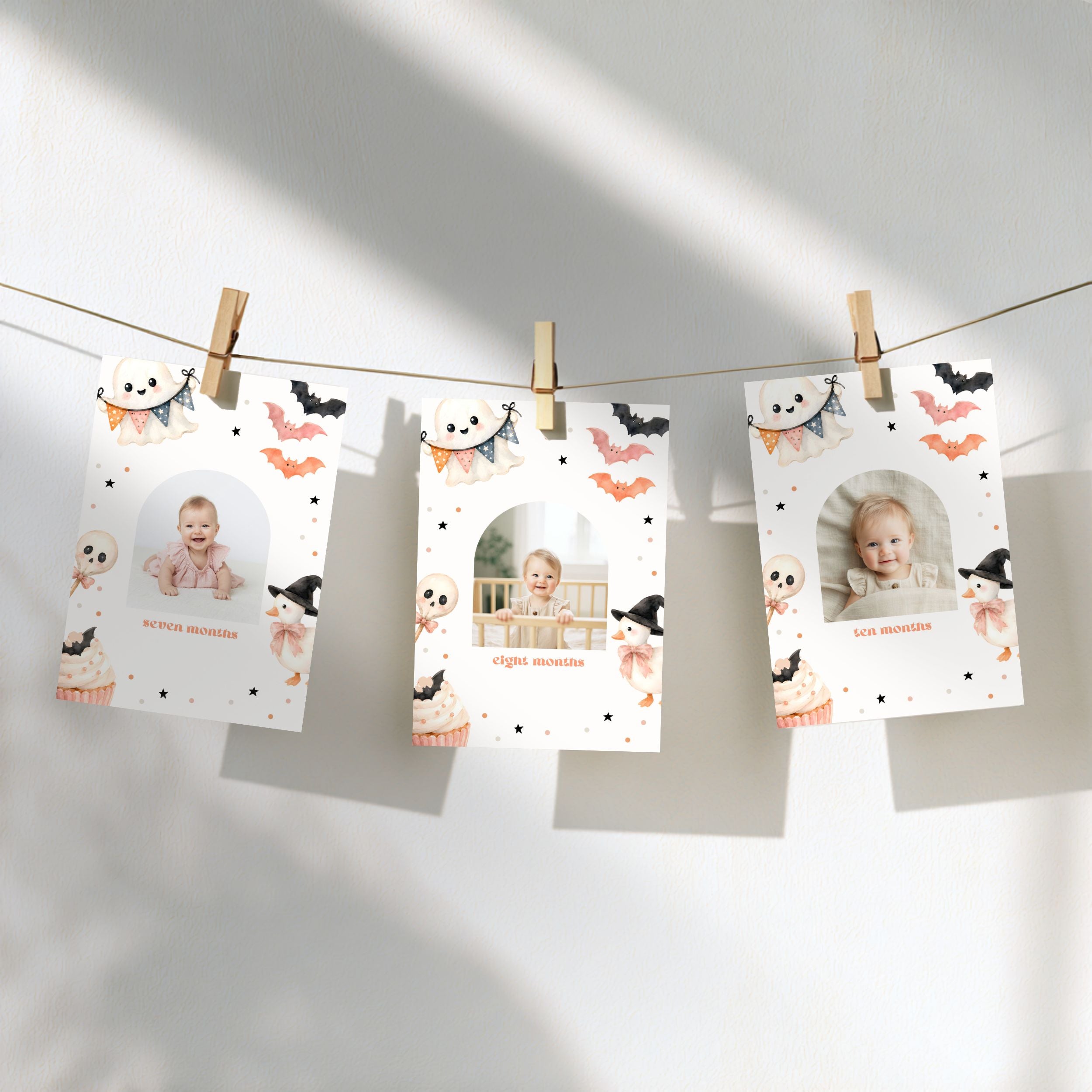 Three personalized Halloween photo cards clipped to a string against a white wall, decorated with cute cartoon illustrations of ghosts, bats, and cupcakes.