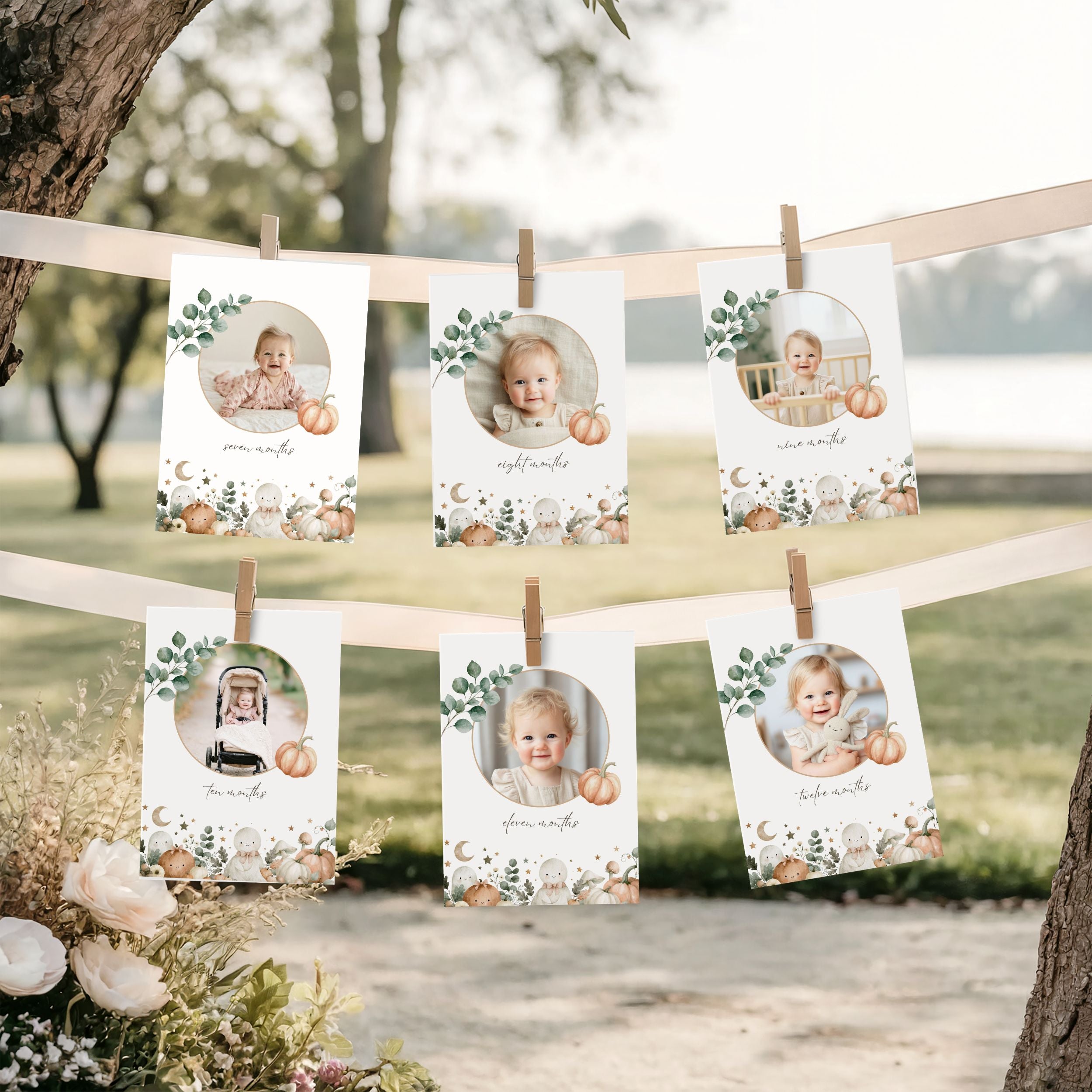 Six printed halloween baby milestone cards with circular photo cutouts, autumn floral and pumpkin borders, and handwritten names, hanging from a string outdoors between trees with flowers at the base.