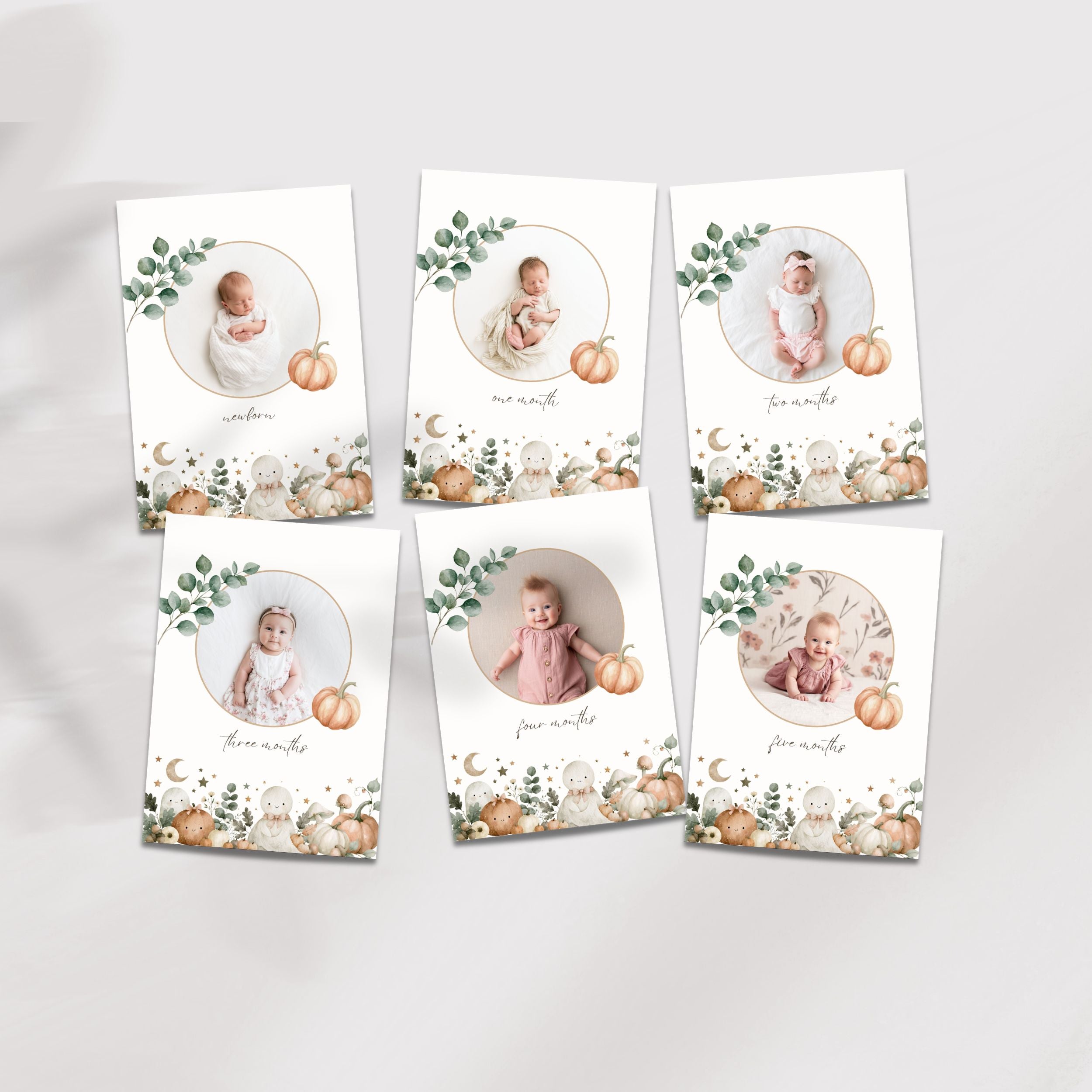 Six halloween baby photo cards arranged in two rows on a light gray background. Each card has a white base with a circular photo frame, green eucalyptus leaves, small pumpkins, and a decorative floral border.
