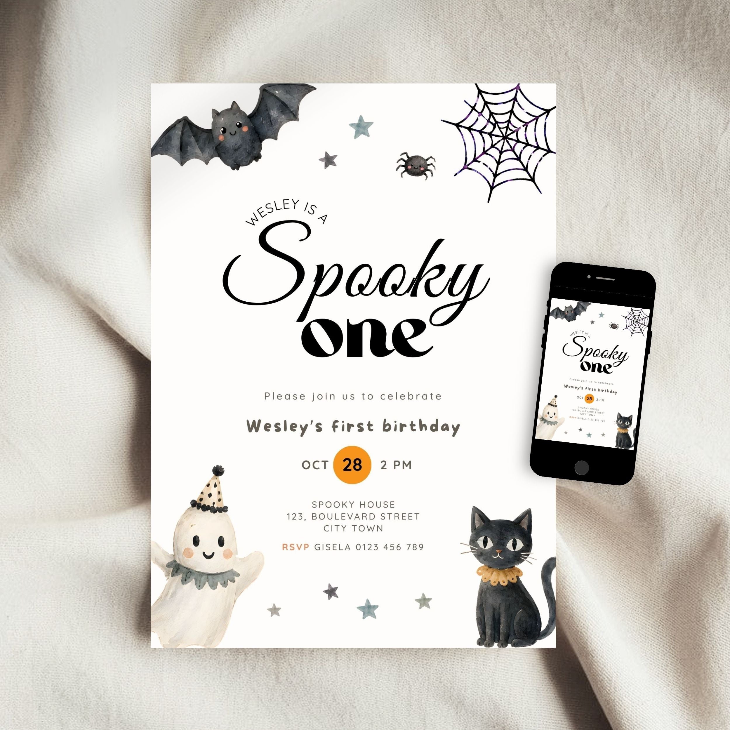 A Halloween-themed birthday invitation card for Wesley's first birthday, styled on a beige fabric background next to a smartphone displaying the digital version of the invitation. The card features black text, illustrations of a bat, spiderweb, spider, ghost, and black cat, with a small orange circle highlighting the date.