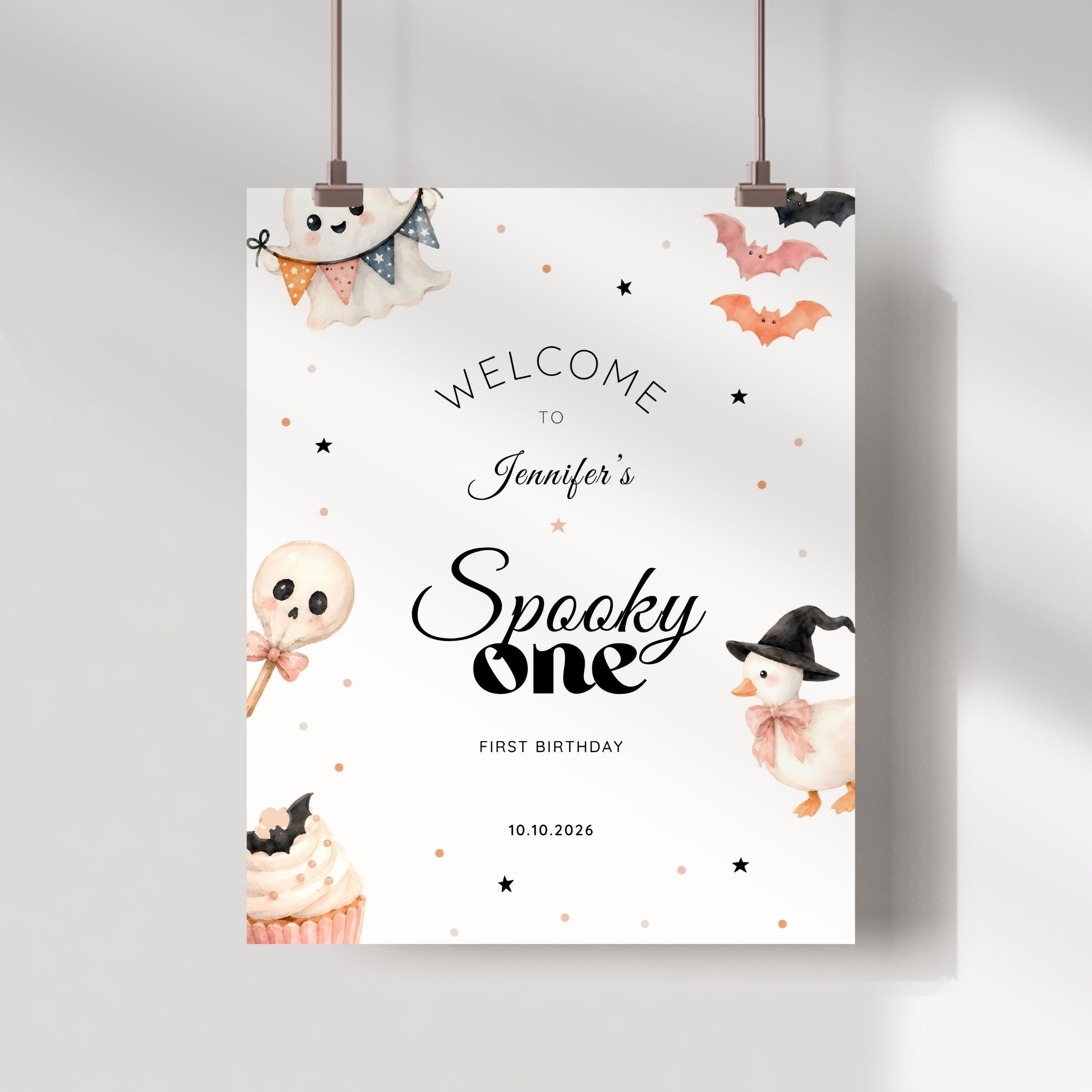 A personalized Halloween party sign hanging from two clips against a light gray wall. The sign has a white background with cute watercolor illustrations of a ghost, cupcake, lollipop, duck, and bats, along with the text 'WELCOME TO Jennifer's Spooky one FIRST BIRTHDAY' and the date '10.