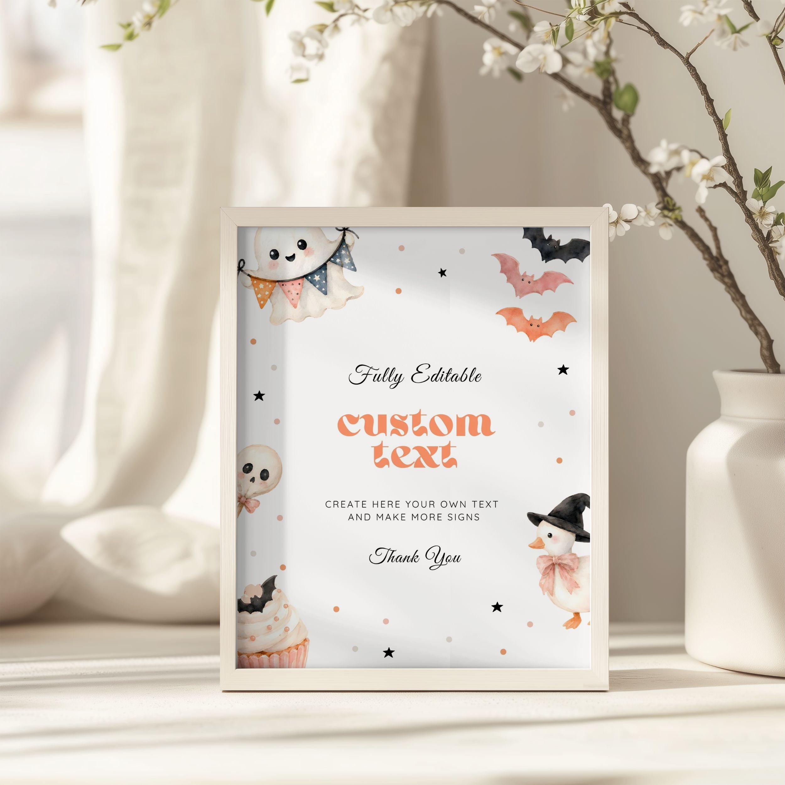 A framed Halloween-themed editable sign mockup standing on a tabletop. The white sign features cute watercolor illustrations of a ghost, pumpkin, bat, snowman, and cupcake, with placeholder text reading 'custom text' and other decorative text.