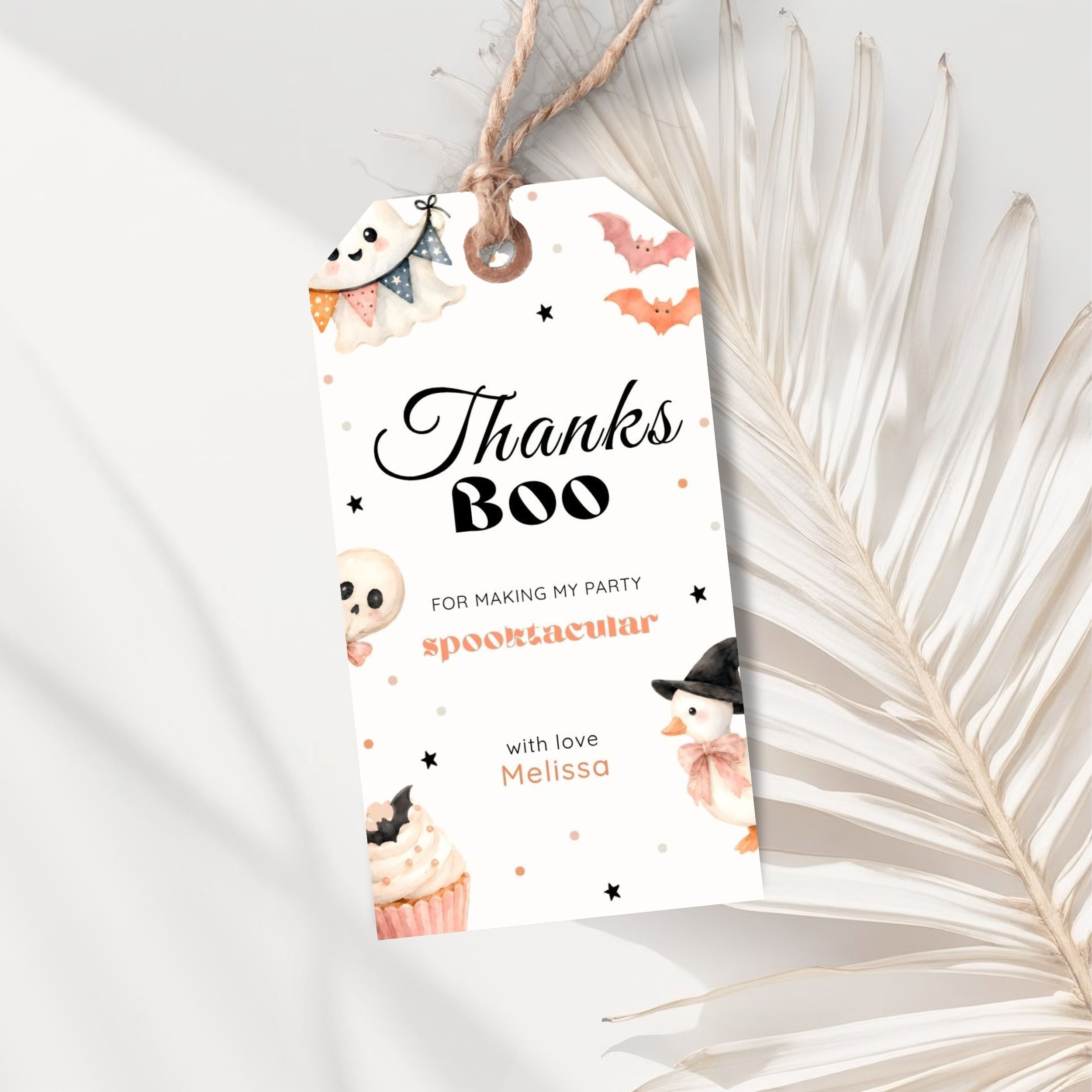 A Halloween-themed gift tag with a rustic twine loop, featuring cute illustrations of a ghost, bat, cupcake, and snowman, with the text 'Thanks Boo' on a white background styled with dried palm leaves.