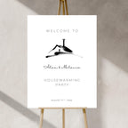 Housewarming party invitation with a black silhouette of a house on a white background, displayed on an easel.