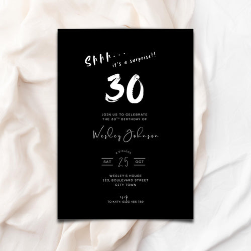 Black 30th birthday invitation card with white text on a white fabric background