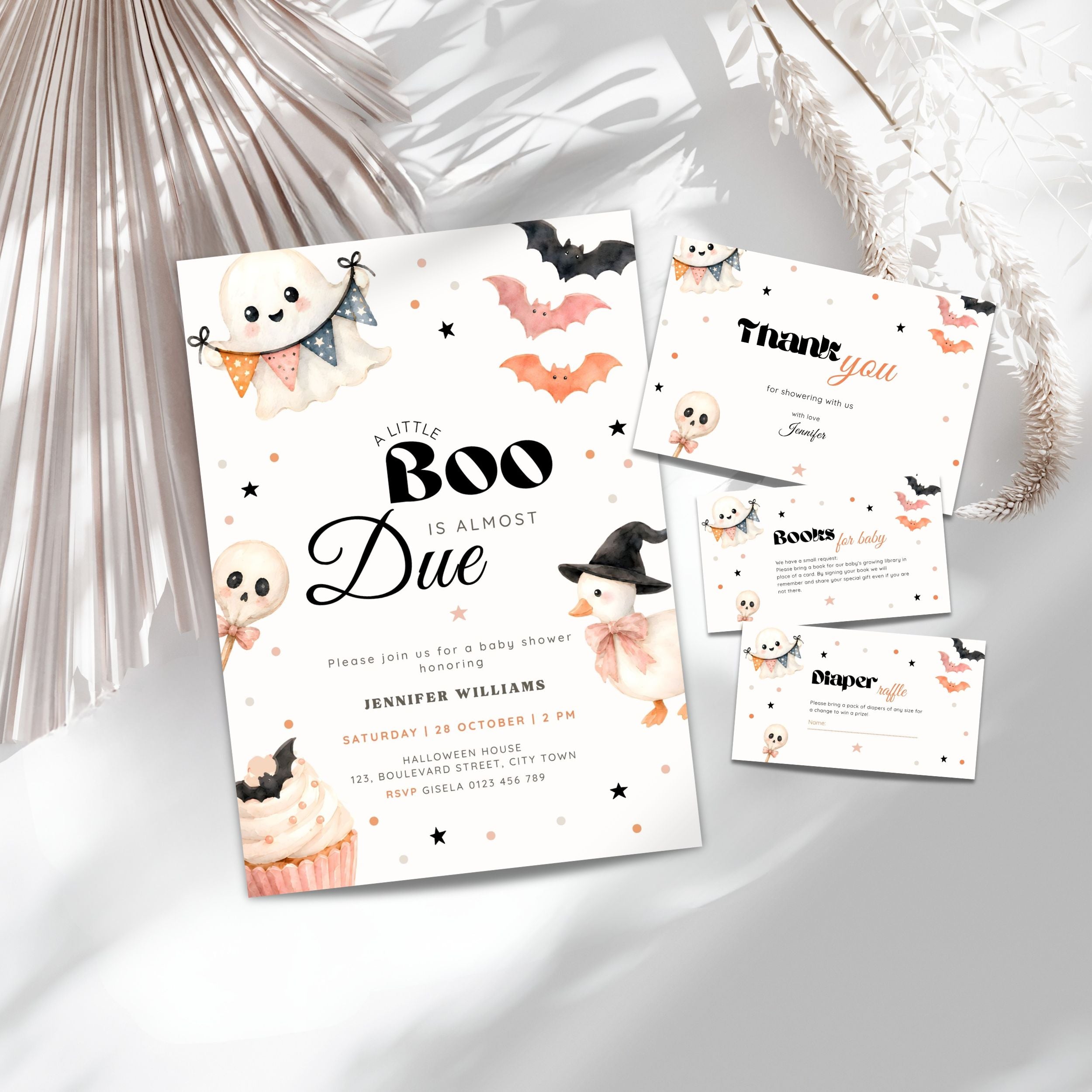 A Halloween baby shower invitation suite styled on a light neutral surface with pink flowers. The main product is a white invitation card featuring black text and cute illustrations of a ghost, cupcake, witch, bats, and stars, alongside a thank-you card, books for baby and a diaper raffle card.