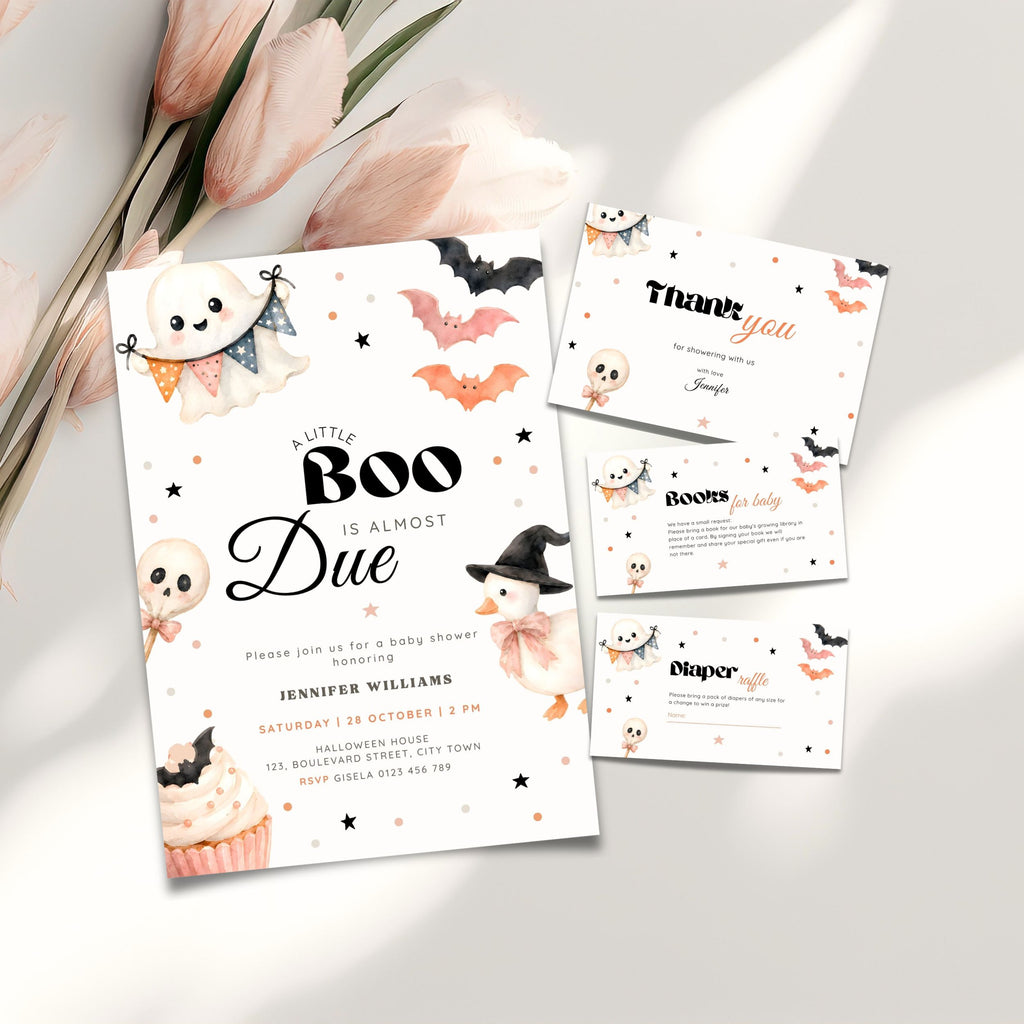 A Halloween baby shower invitation suite styled on a light neutral surface with pink flowers. The main product is a white invitation card featuring black text and cute illustrations of a ghost, cupcake, witch, bats, and stars, alongside a thank-you card, books for baby and a diaper raffle card.