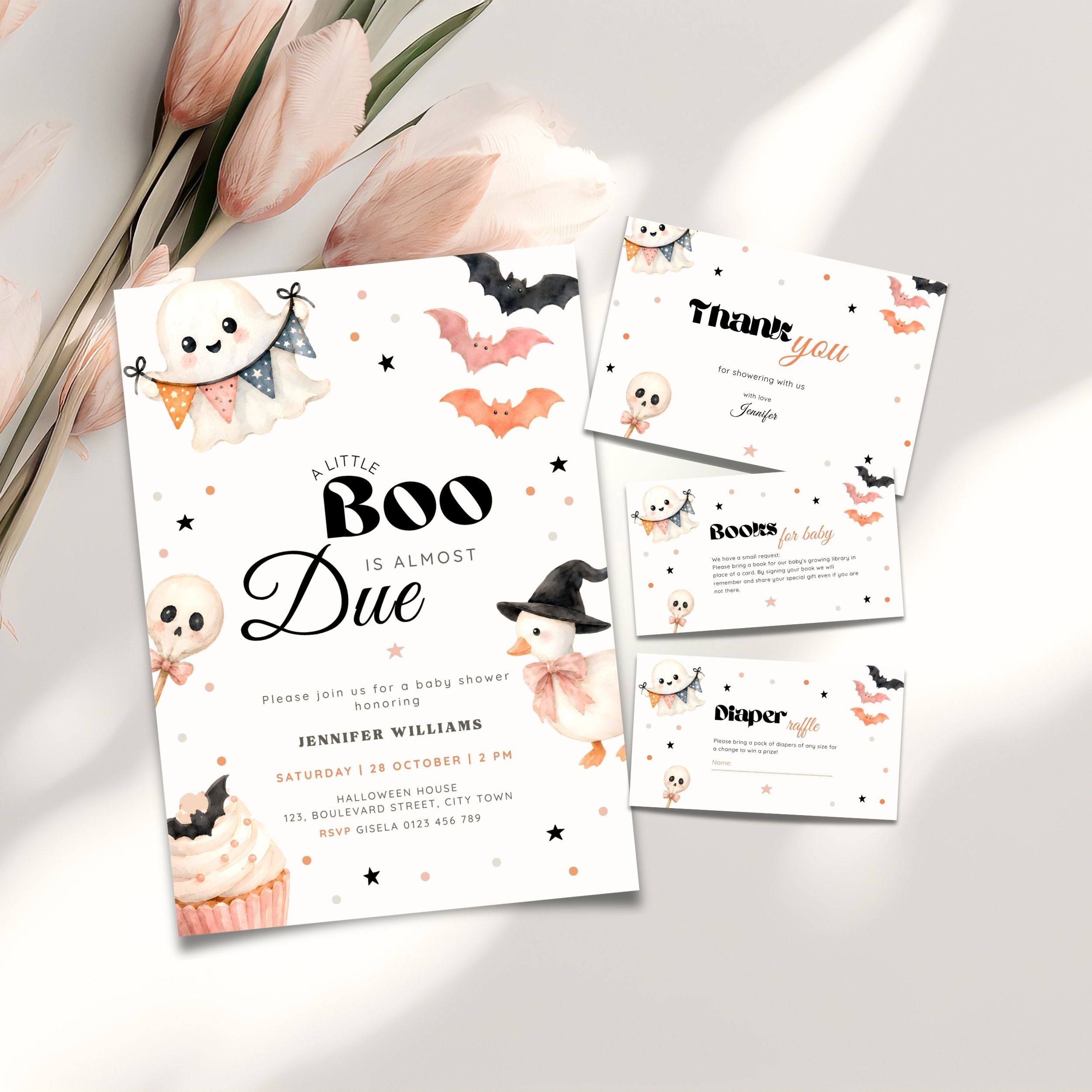 A Halloween baby shower invitation suite styled on a light neutral surface with pink flowers. The main product is a white invitation card featuring black text and cute illustrations of a ghost, cupcake, witch, bats, and stars, alongside a thank-you card, books for baby and a diaper raffle card.
