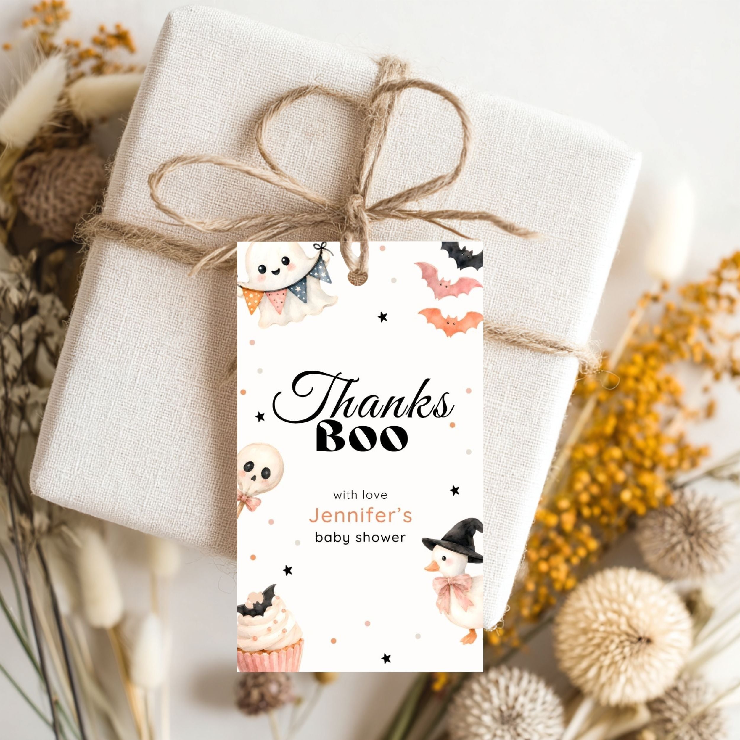 A wrapped gift box tied with twine and adorned with a Halloween-themed 'Thanks Boo' gift tag, styled with dried flowers on a light background.