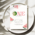 A watercolor-style first birthday invitation card featuring pink 'ONE in a millen' text and watermelon illustrations, styled on a speckled ceramic plate with soft shadows.