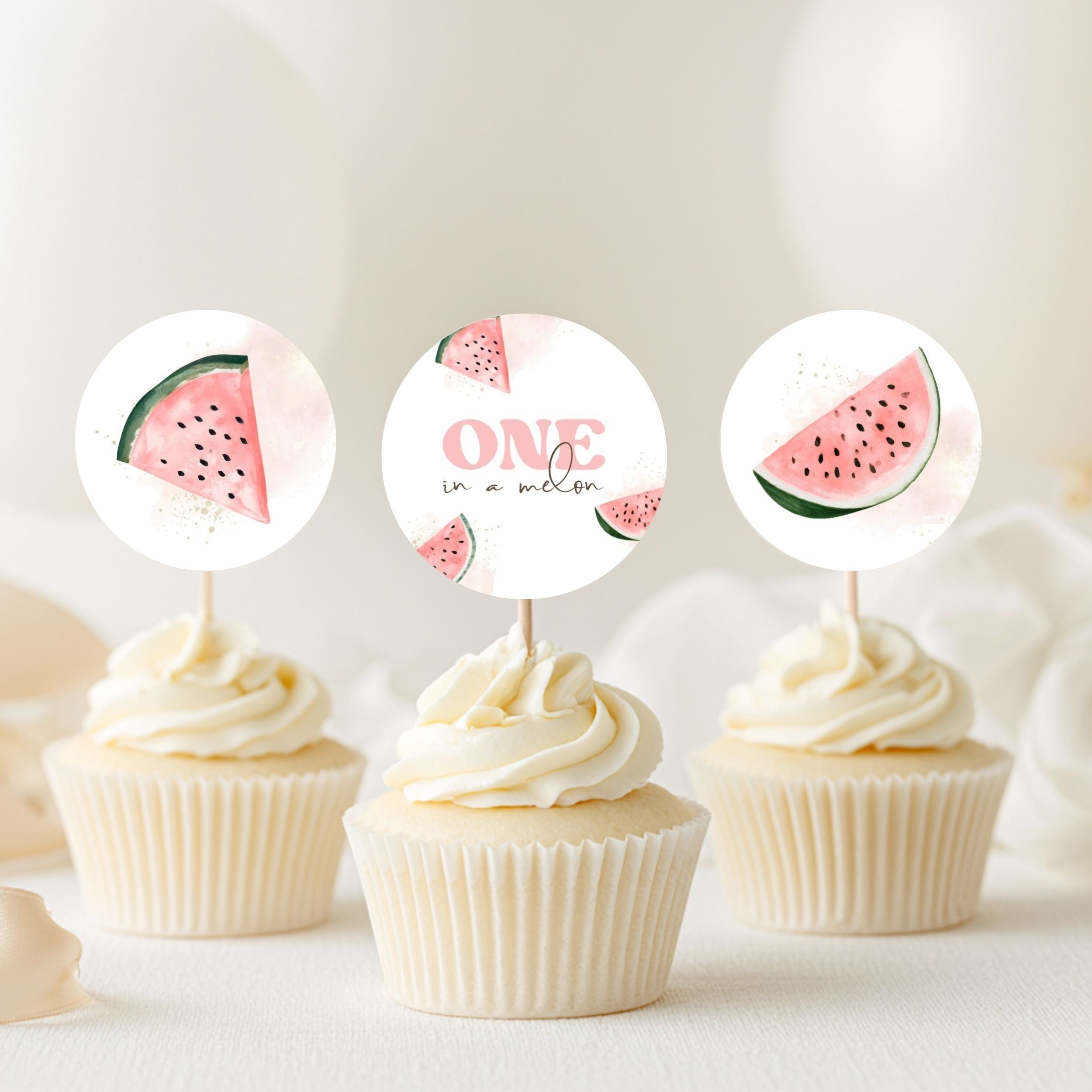 Three watercolor-style cupcake toppers with pink watermelon slices and the words 'ONE in a melon' are displayed on top of three frosted cupcakes against a soft, light background.