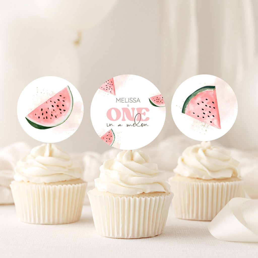 Three watercolor watermelon cupcake toppers displayed on top of white-frosted cupcakes against a soft, light beige background.