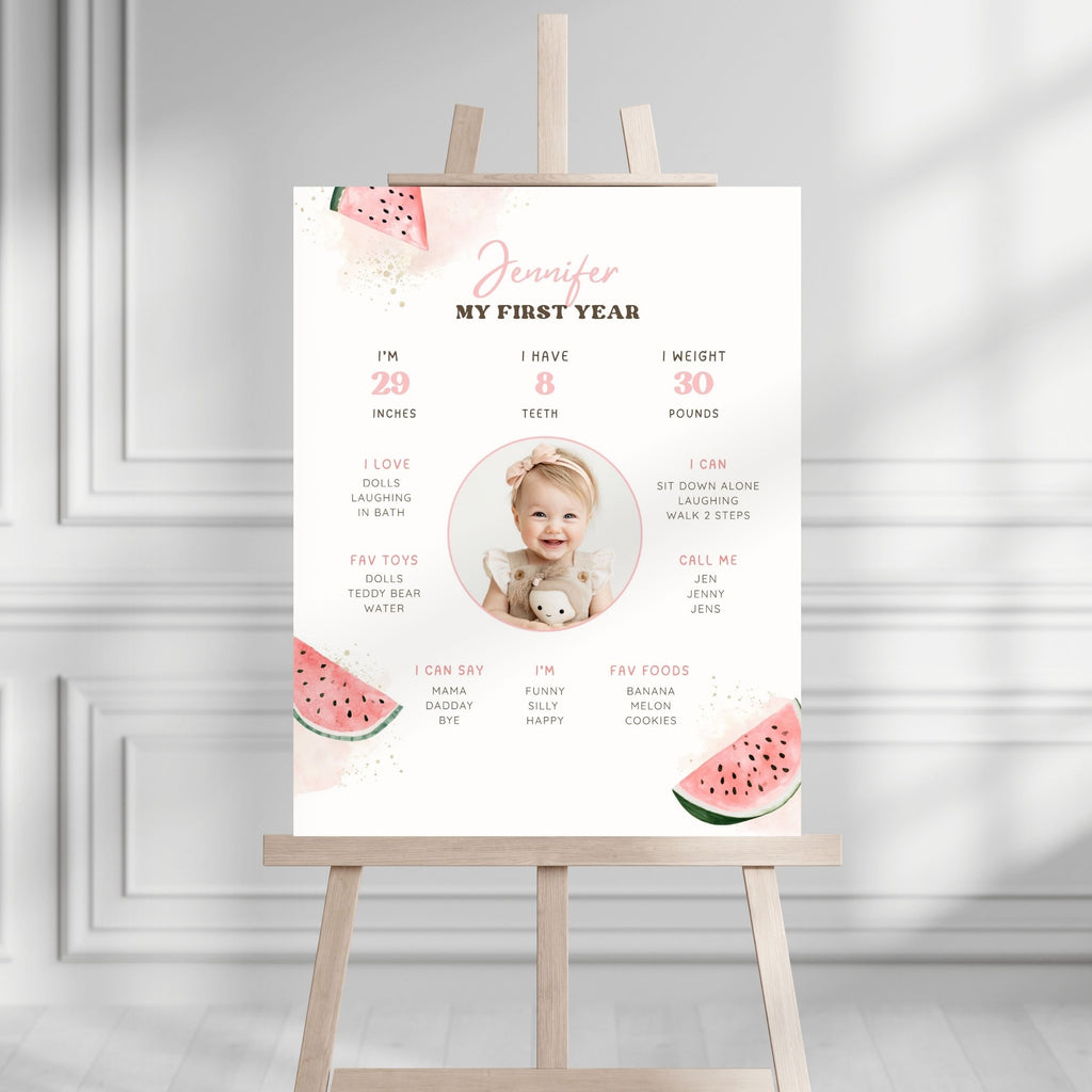 A personalized baby milestone poster for 'Jennifer' displayed on a wooden easel. The white poster features pink and green watermelon graphics, a central photo placeholder of a baby, and cute text detailing baby milestones in a clean, modern room setting.