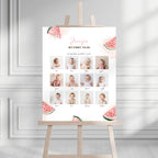A personalized baby milestone sign on an easel, featuring watermelon illustrations and a grid of baby photos with names and ages, set against a white paneled wall background.
