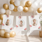 Three personalized photo cards clipped to a string with wooden clothespins, decorated with watermelon graphics and milestone text, set against a soft background of gold and white balloons.