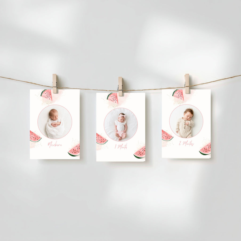 Three baby milestone photos printed on white cards with watermelon illustrations, hanging from a string with wooden clothespins against a soft light gray background.