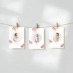 Three baby milestone photos printed on white cards with watermelon illustrations, hanging from a string with wooden clothespins against a soft light gray background.