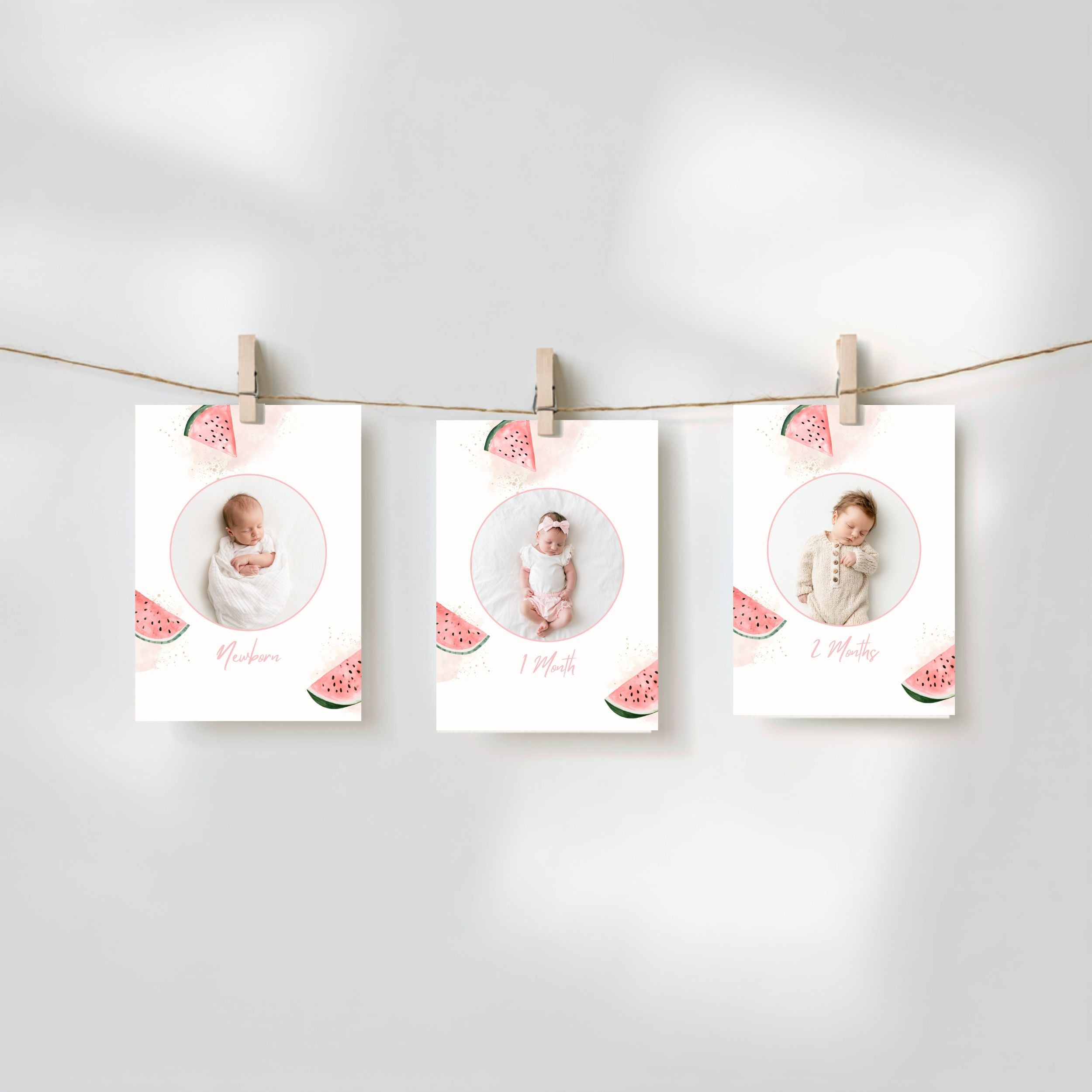 Three baby milestone photos printed on white cards with watermelon illustrations, hanging from a string with wooden clothespins against a soft light gray background.