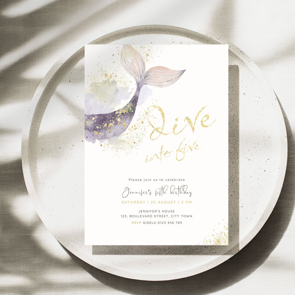 A square birthday invitation card featuring a watercolor mermaid tail design in purple, pink, and gold, with gold script text reading 'Dive into five' and black event details below, styled on a speckled white plate with soft leaf shadows.