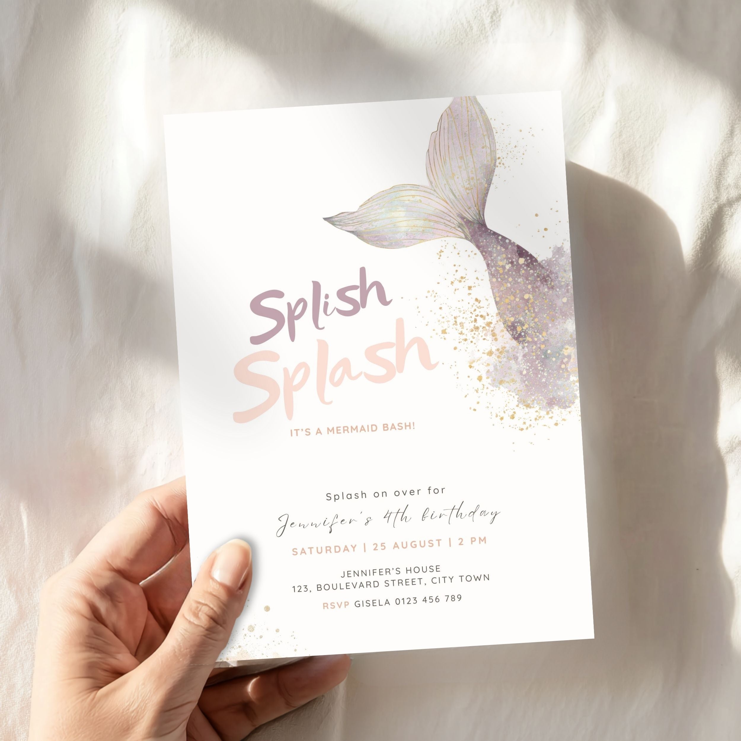 A hand holds a mermaid-themed birthday invitation card featuring a watercolor mermaid tail design and the text 'Splash Splash' on a soft white fabric background.
