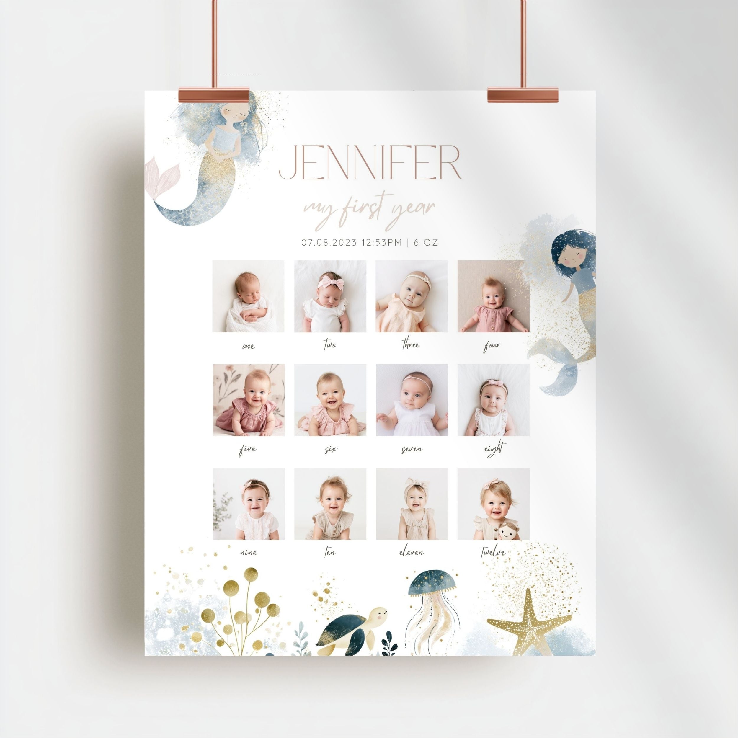 A personalized baby first-year photo calendar poster hanging from two copper clips against a light gray wall. The white poster features the name 'JENNIFER' and 'my first year' in elegant typography, a grid of 12 baby photos from infancy, and whimsical watercolor illustrations of a mermaid, jellyfish, starfish, and sea life in soft pastel tones.