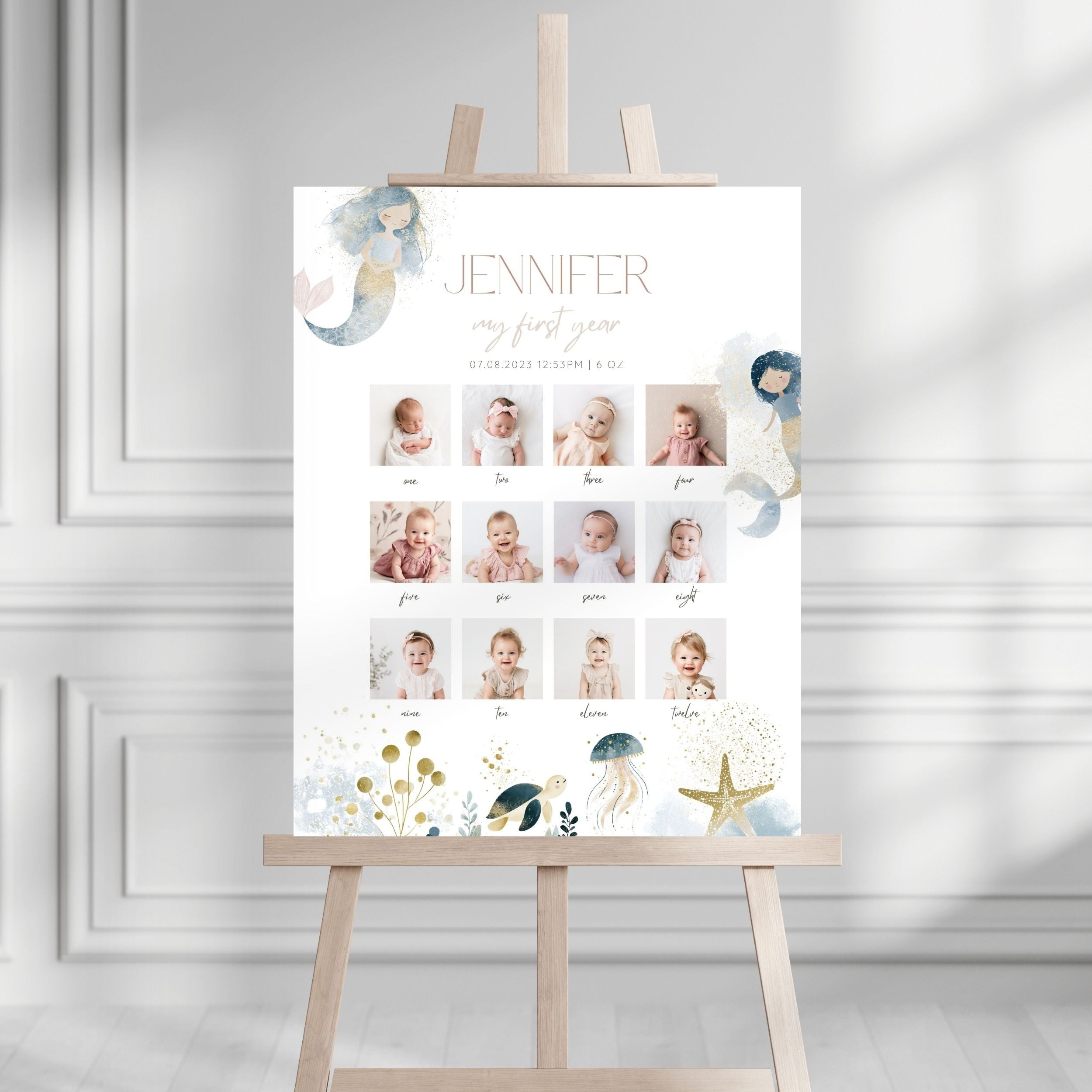 A personalized baby first-year photo timeline sign displayed on a wooden easel. The white sign features the name 'JENNIFER', 'my first year', and a grid of baby photos with labels.