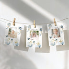 Three printed milestone photos hang from a string with wooden clothespins against a white wall. The cards have a soft blue and gold seashell and starfish illustration design, with baby photos shown in the center slots.