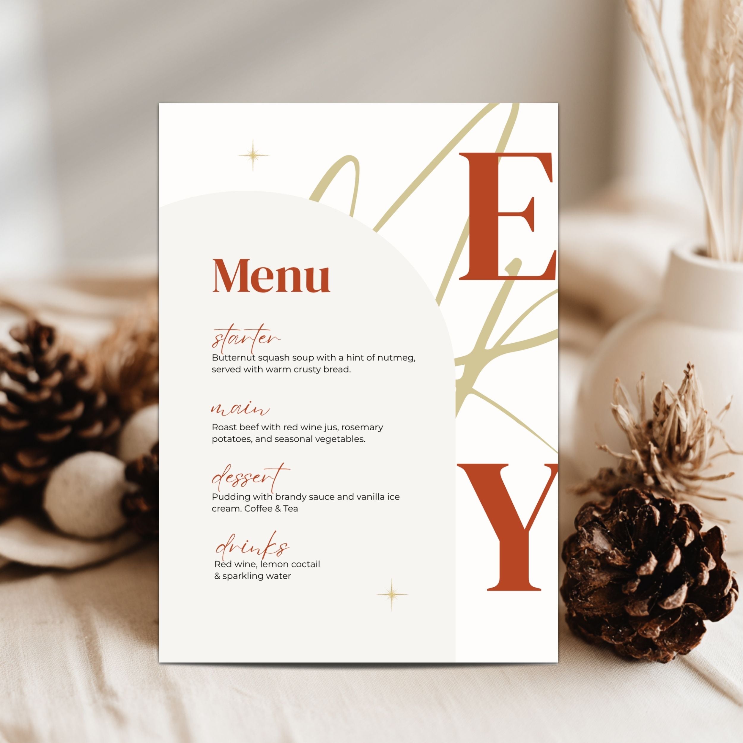 A vertical christmas menu card displayed upright on a light fabric surface, surrounded by decorative pinecones and dried grass in a soft neutral setting. The card has a warm off-white background with large rust-red serif letters 'E' and 'Y' and small gold abstract line accents, plus a printed menu title 'Menu' and small course text.