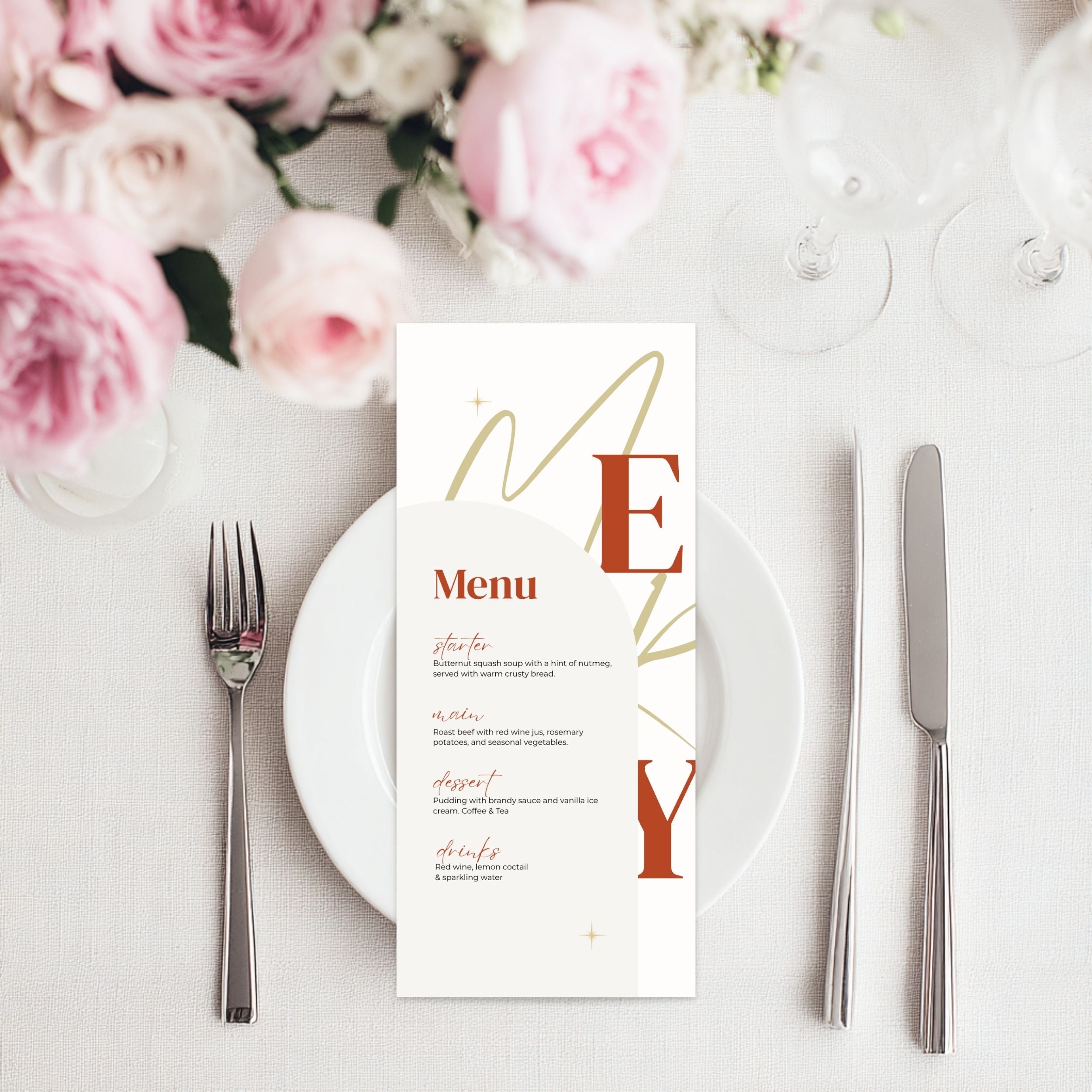 A christmas menu card with elegant typography and gold monogram details, styled on a white plate with silver cutlery and pink roses in the background.