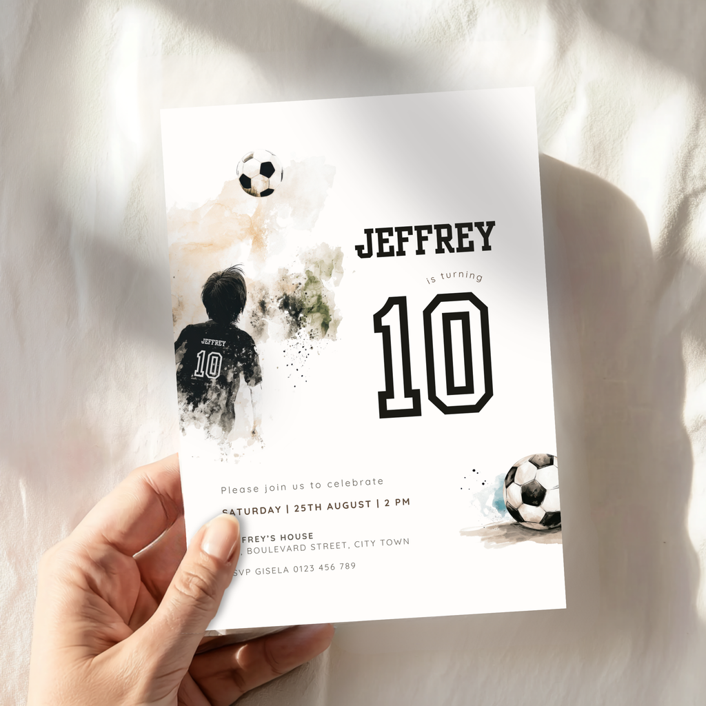 A hand holds a white soccer-themed 10th birthday invitation card featuring the name JEFFREY, the number 10, and watercolor-style soccer graphics, set against a soft white fabric background with natural shadows.