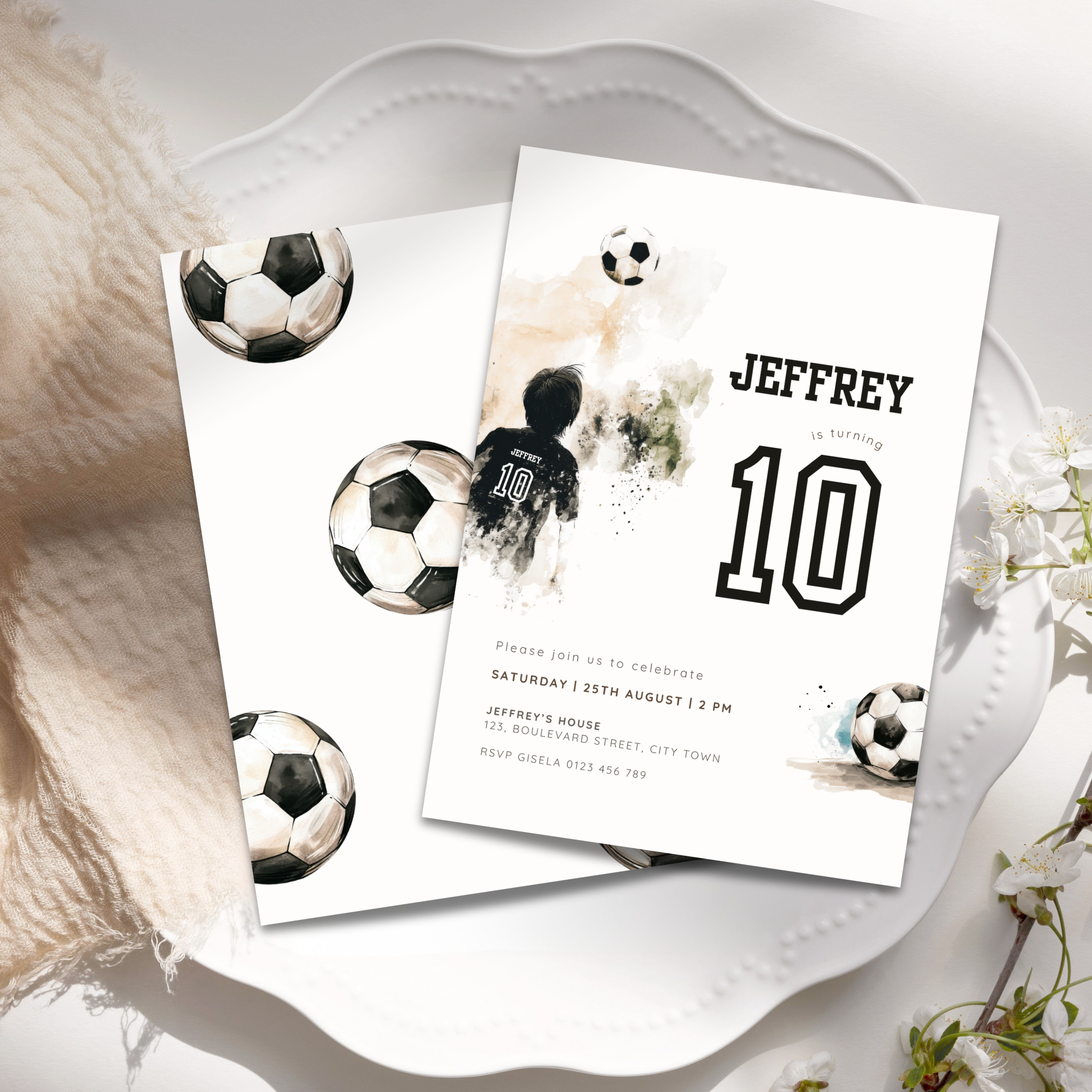 A soccer-themed 10th birthday invitation card displayed on a white decorative tray with a soft beige blanket and small white flowers. The card features watercolor soccer balls, a child in a soccer jersey, and the text 'JEFFREY is turning 10'.