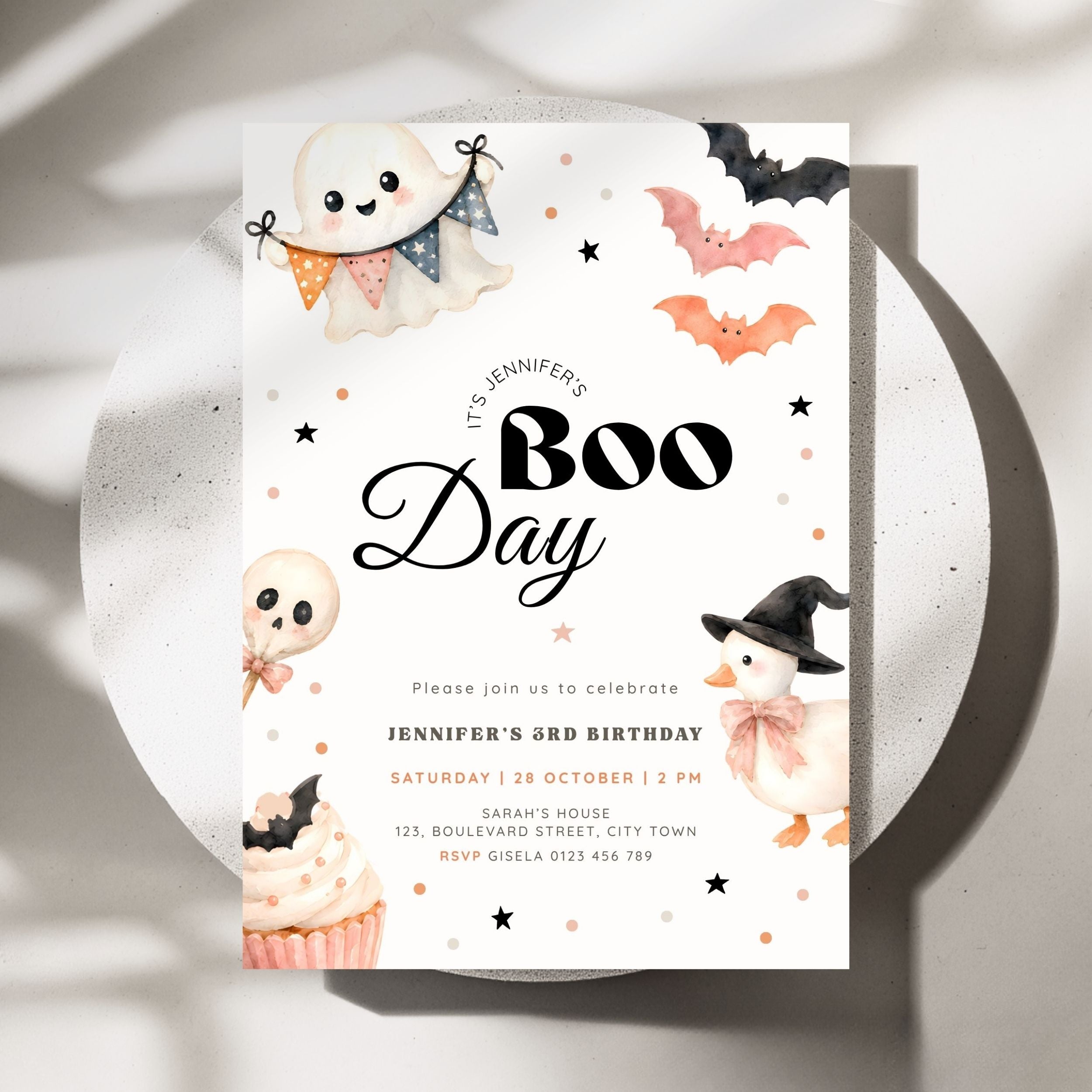 A Halloween-themed birthday invitation card for 'Boo Day' featuring cute watercolor illustrations of a ghost, bats, a skull lollipop, a cupcake, and a witch hat on a white background, styled on a round white plate with soft shadows.