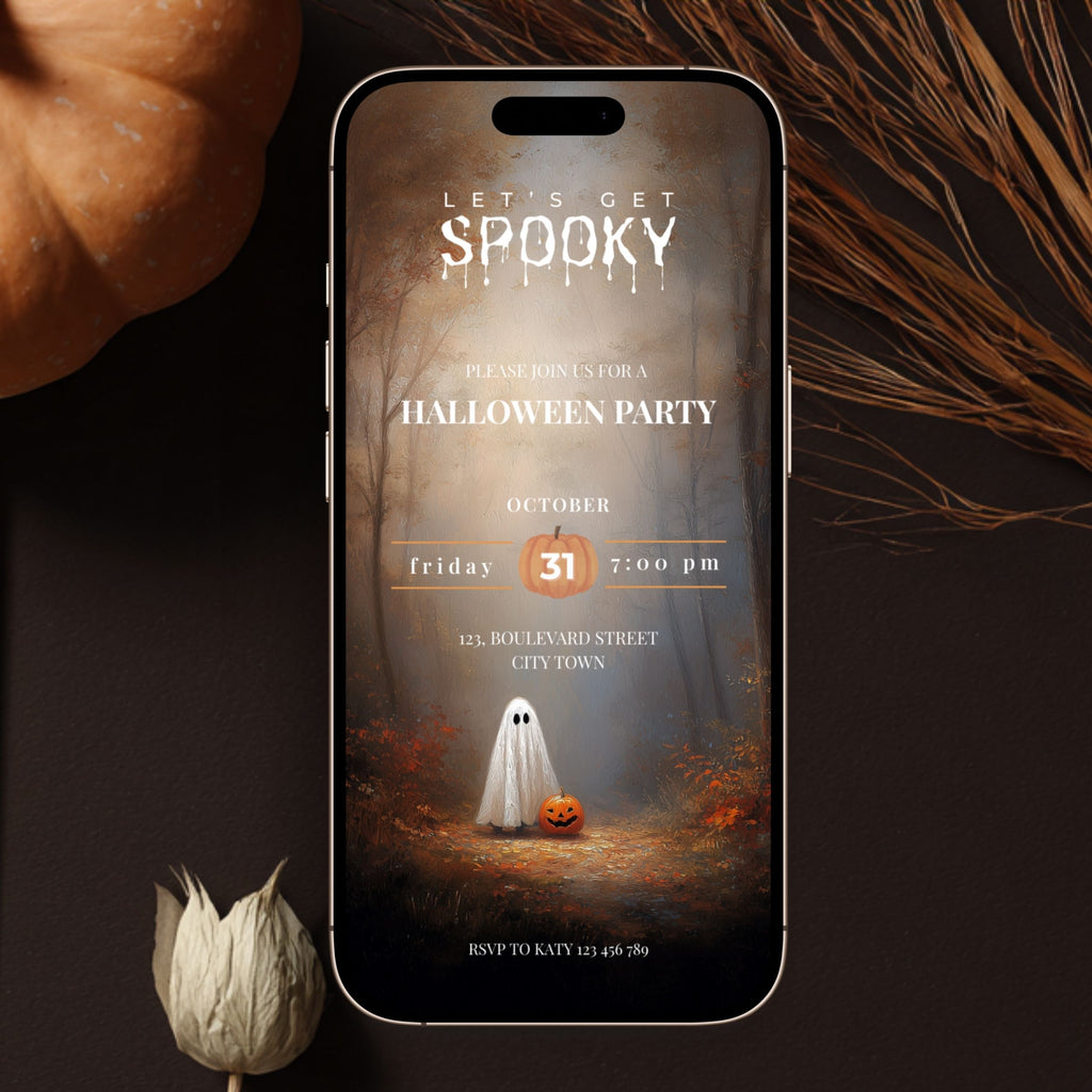 A smartphone centered on a dark surface, displaying a Halloween party invitation design with a ghost, pumpkin, and autumn forest scene. Decorative dried grass and a small flower are placed around the phone.