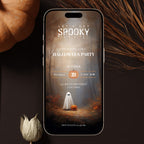 A smartphone centered on a dark surface, displaying a Halloween party invitation design with a ghost, pumpkin, and autumn forest scene. Decorative dried grass and a small flower are placed around the phone.