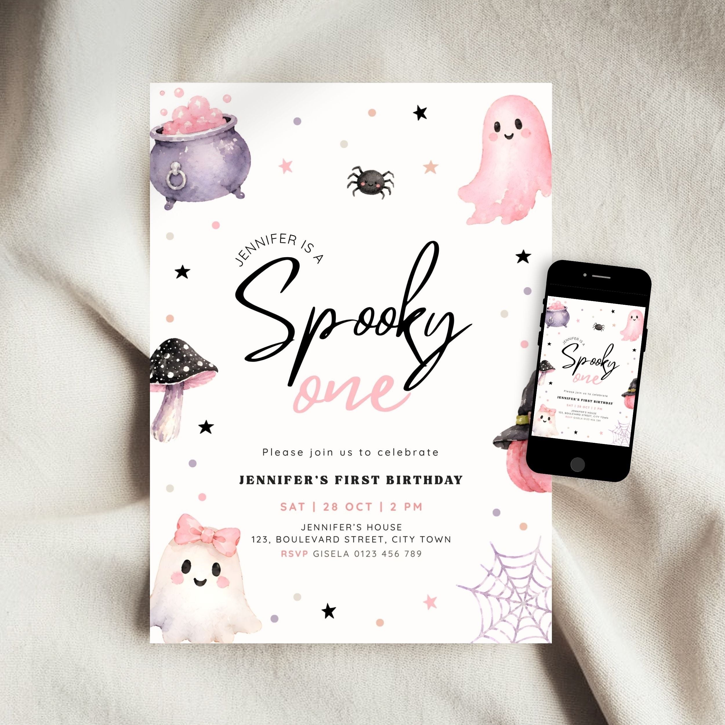 A Halloween-themed first birthday invitation card displayed on a soft beige fabric surface next to a smartphone showing the same design on screen. The card features cute watercolor illustrations of a ghost, cauldron, mushroom, spider, and web with the text 'Jennifer is a Spooky one' and event details.