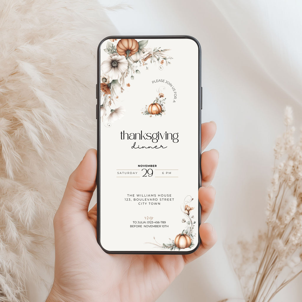 A hand holds a smartphone displaying a Thanksgiving dinner invitation design with floral autumn illustrations, set against a soft beige textured background with dried grasses.
