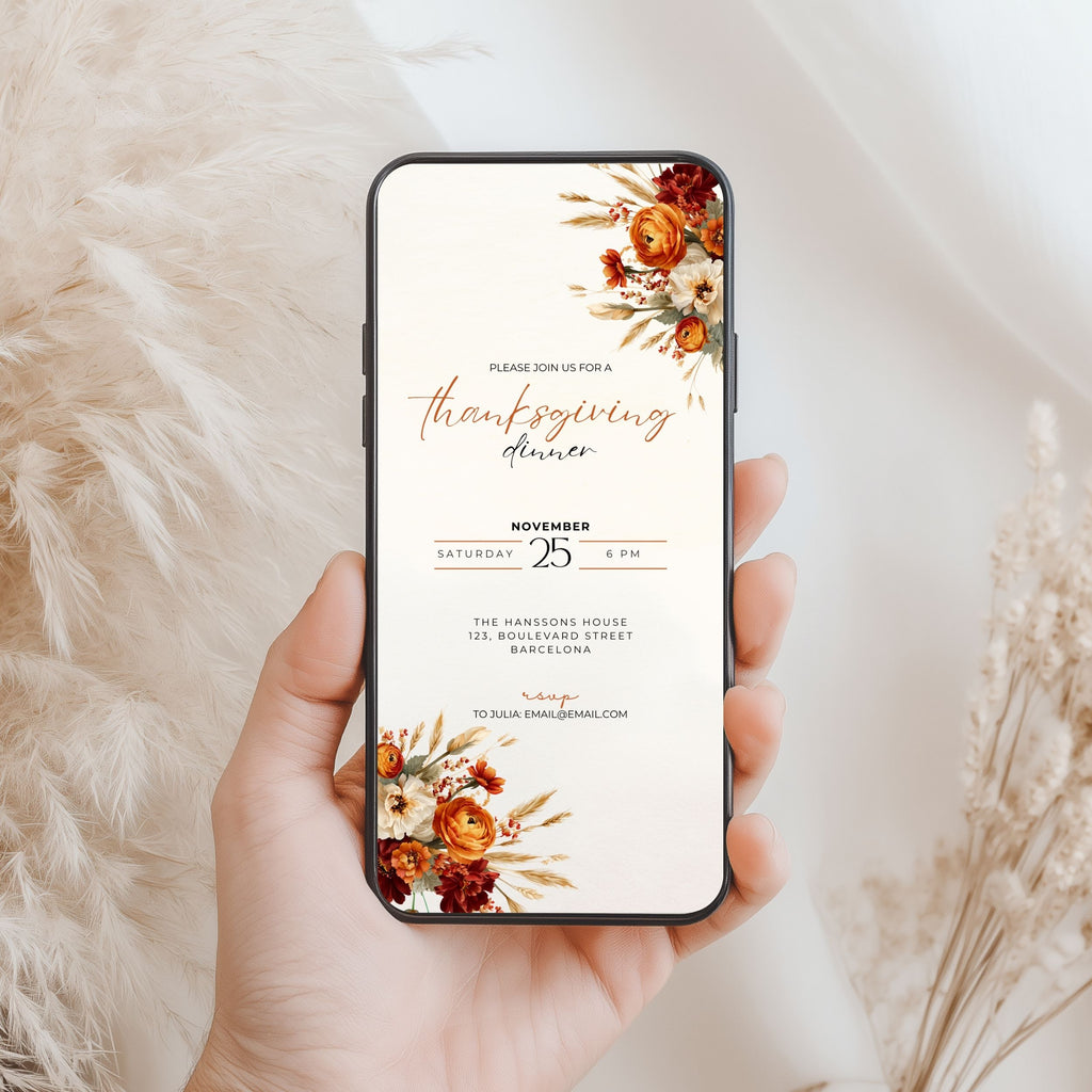A hand holds a smartphone displaying a Thanksgiving dinner invitation design with floral illustrations in warm autumn tones, set against a soft beige background with dried grasses.