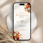 A smartphone centered on a white plate, displaying a Thanksgiving dinner invitation design with floral illustrations in warm autumn tones. The phone is styled on a beige fabric surface with dried grass accents.
