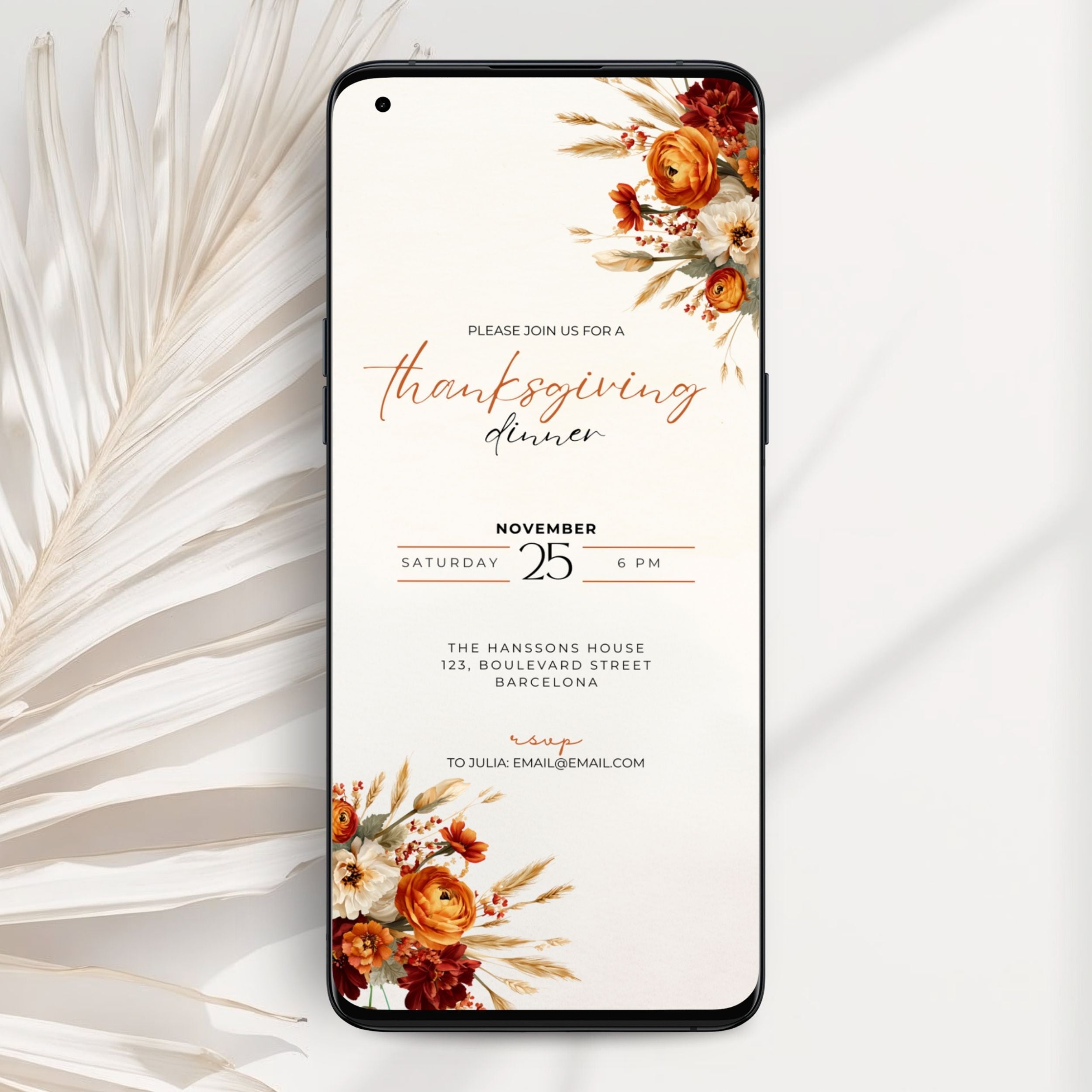 A smartphone mockup displaying a Thanksgiving dinner invitation card with floral autumn illustrations in orange, rust, and cream on a white background, styled with dried palm leaves.