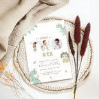 A personalized dinosaur-themed 2nd birthday invitation card styled in a flat lay on a white woven placemat with a beige knit blanket, dried grass stems, and small orange flowers.