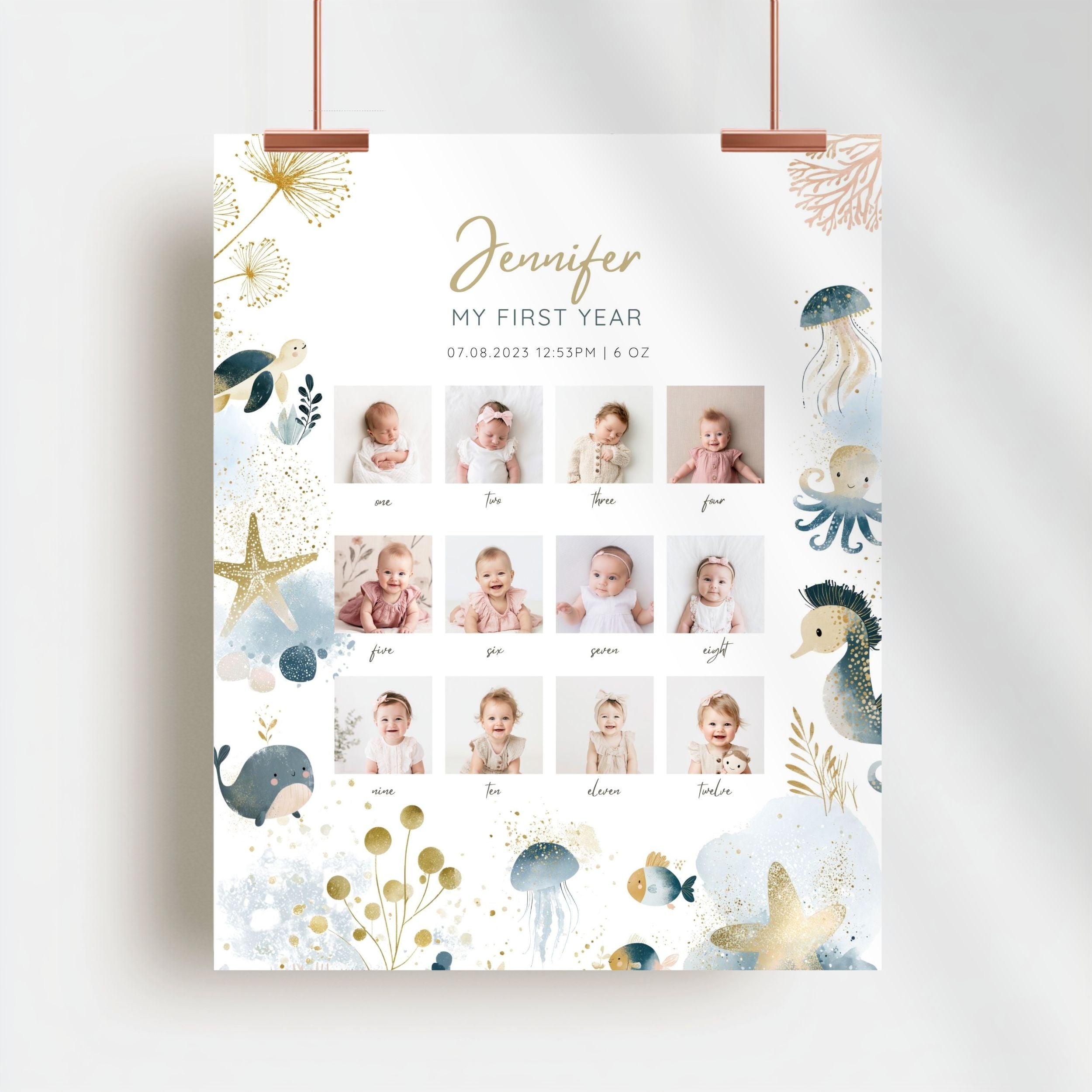 A personalized baby first year photo poster hanging from two copper clips against a white wall. The poster features a white background decorated with watercolor-style sea creatures like a whale, octopus, seahorse, and starfish in blue, gold, and beige.