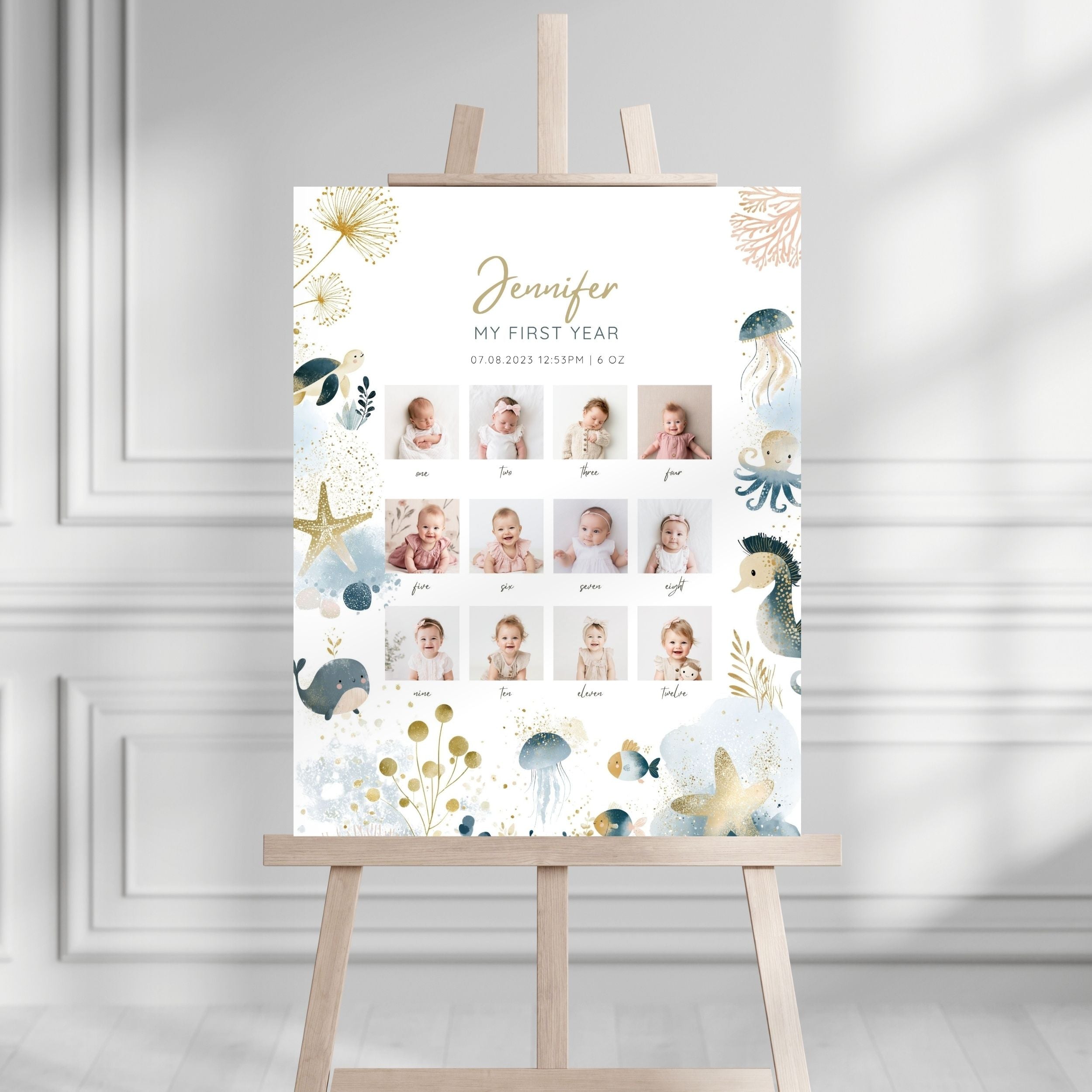 A personalized first-year baby photo gallery sign with an ocean-themed watercolor design, displayed on a wooden easel in a bright, modern room.