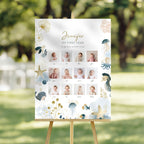 A personalized first birthday reception签到 board displayed on a wooden easel in an outdoor garden setting. The board features a white background decorated with light blue and gold sea-themed illustrations, including jellyfish, starfish, seahorses, and dandelions.