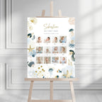 A personalized baby first-year photo wall display on a wooden easel, featuring a white background with gold and blue sea-themed illustrations and a grid of baby photos.