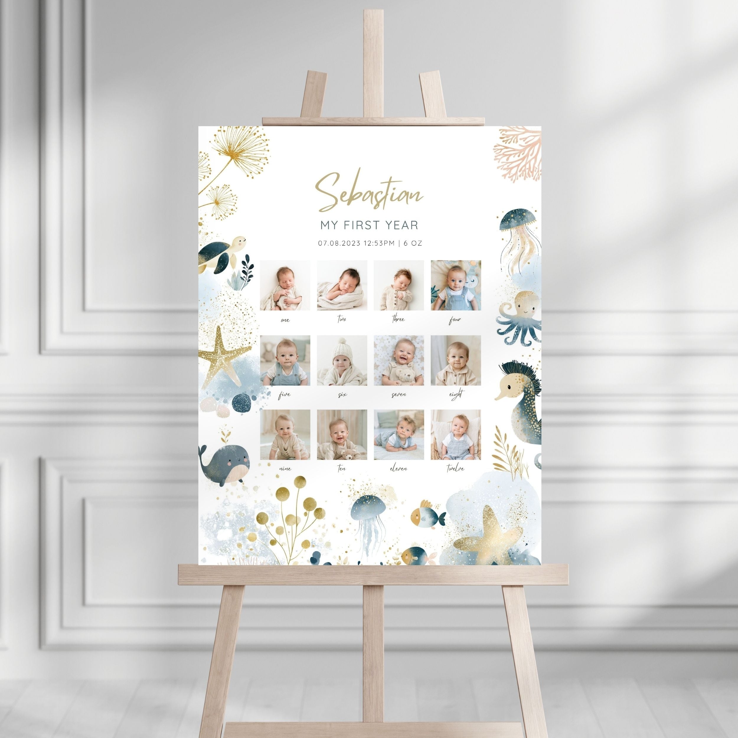 A personalized baby first-year photo wall display on a wooden easel, featuring a white background with gold and blue sea-themed illustrations and a grid of baby photos.